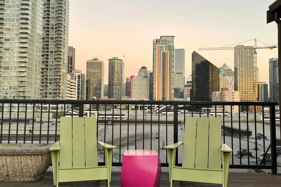 Two Adirondack chairs on the building’s rooftop deck, facing the downtown Seattle skyline in evening light