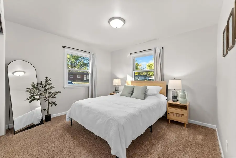 Bedroom with a queen bed, white bedding, an arched floor mirror, and a potted tree