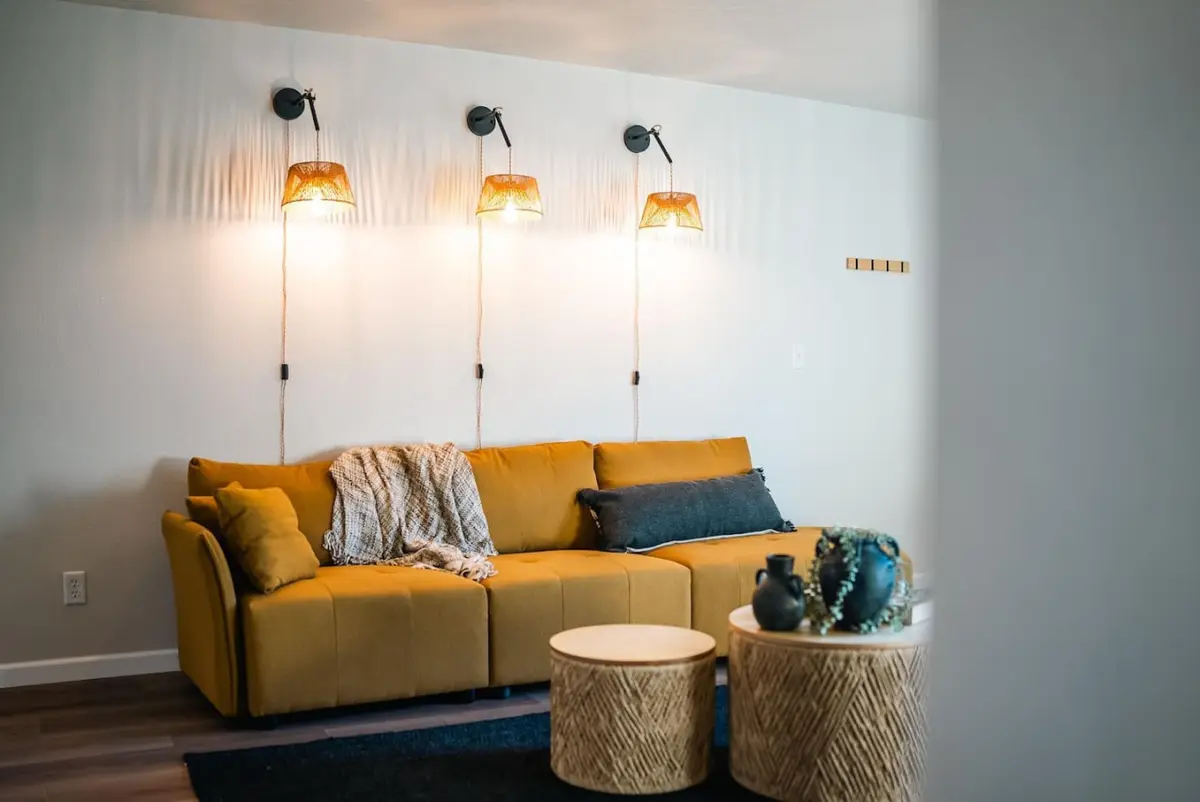Mustard sofa under three lit wall sconces, with round woven side tables