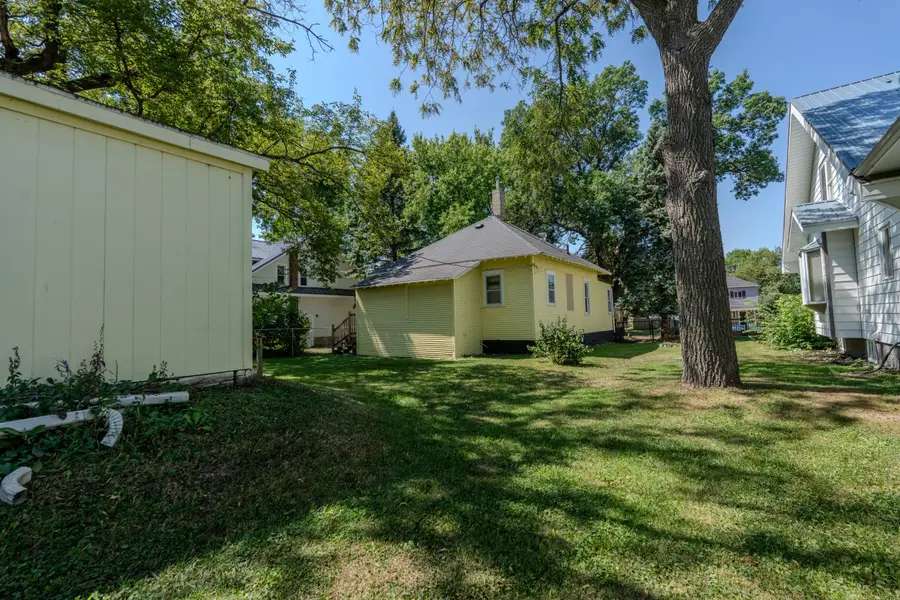 Main Street Cottage, a yellow house seen across a backyard shaded by mature trees