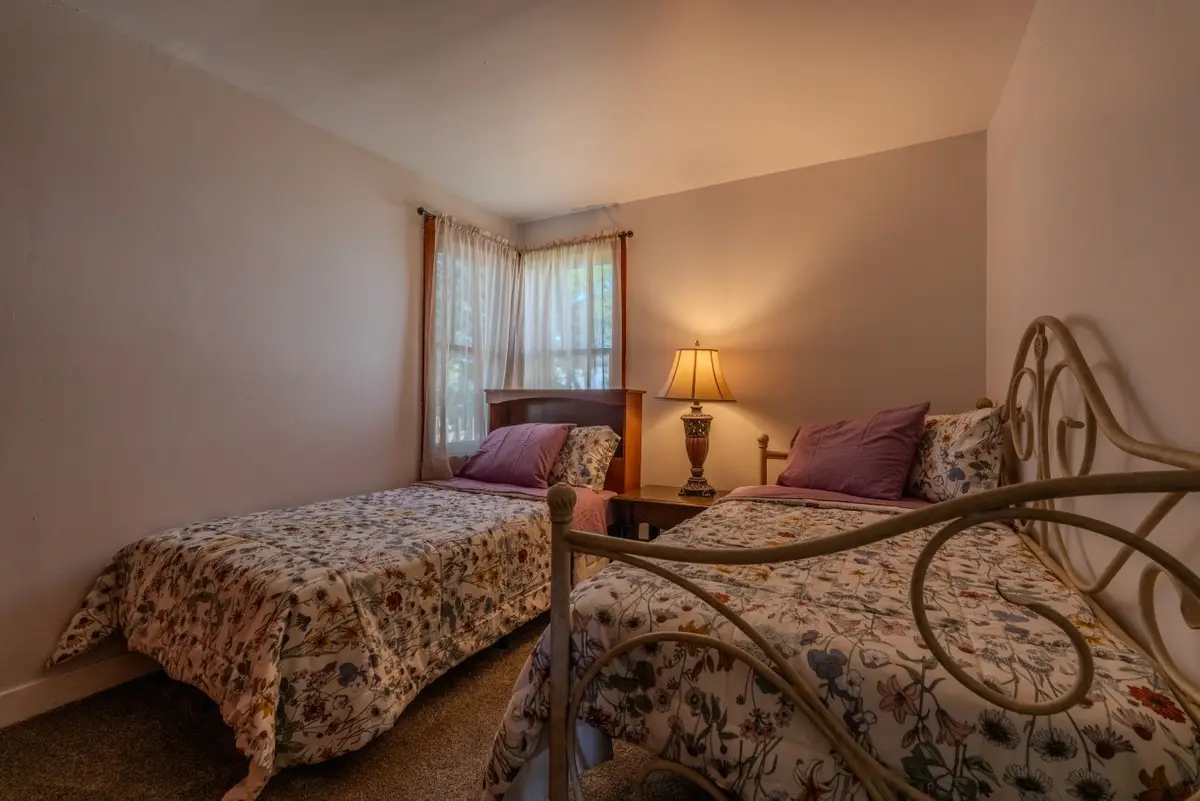 Bedroom with two twin beds in floral bedding, one with a white iron frame, under a corner window