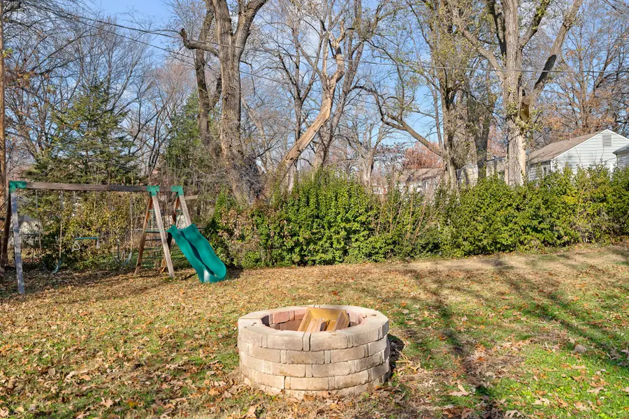 Stone fire pit on the lawn, with a swing set and slide behind