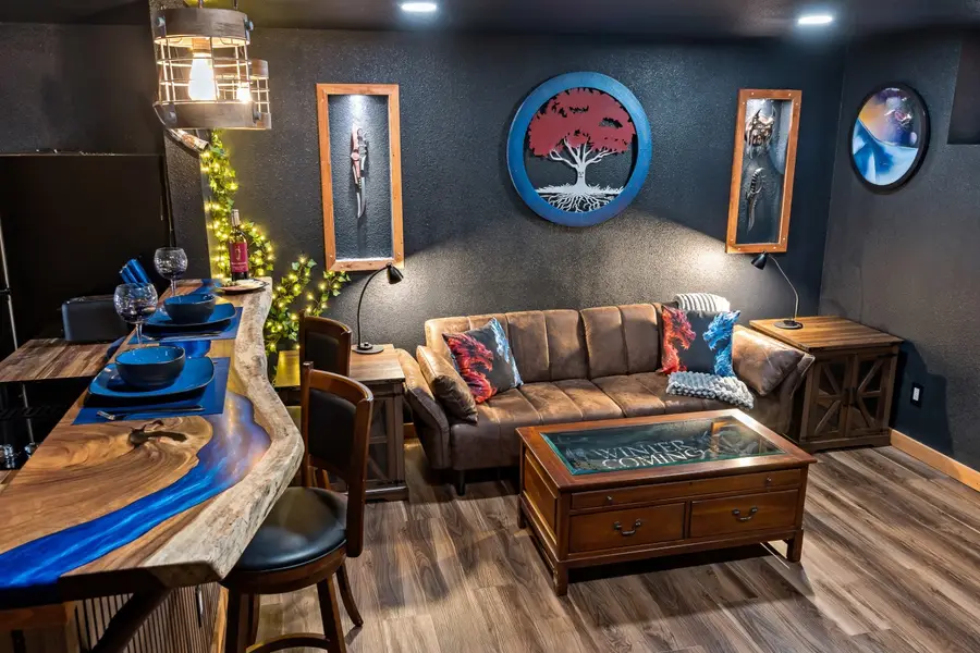 Fantasy-themed lounge with a blue epoxy river bar, a sofa, and lit weapon displays