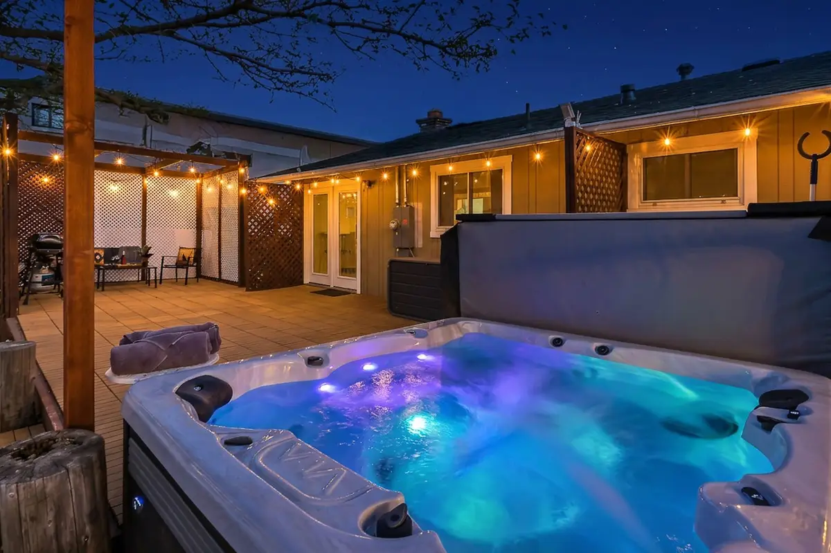 Hot tub lit blue at night under string lights on the deck