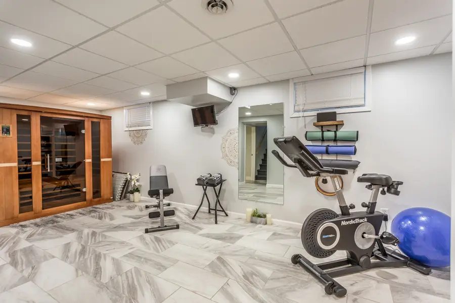 Lower-level gym with a spin bike, a weight bench, and the infrared sauna