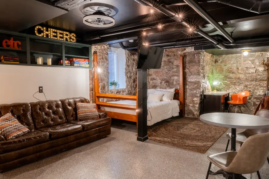 1925 Speakeasy studio with a leather Chesterfield, a four-poster queen bed, and stone walls