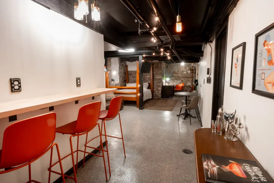 Bar counter with three orange stools under track lights, with the studio beyond