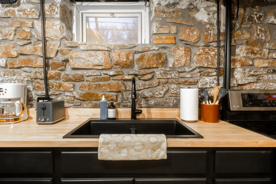 Butcher block counter and black sink set against the original stone wall