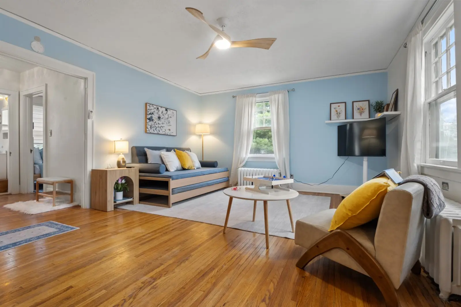 Living room with soft blue walls, oak floors, a twin daybed with trundle, and a reading chair