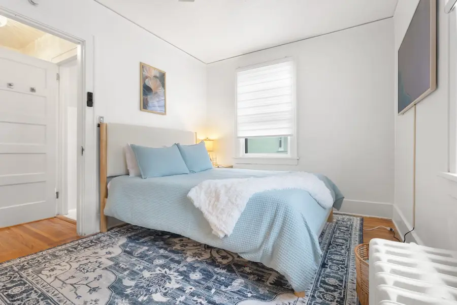 Bedroom with a queen bed in soft blue, a patterned rug, and an original radiator