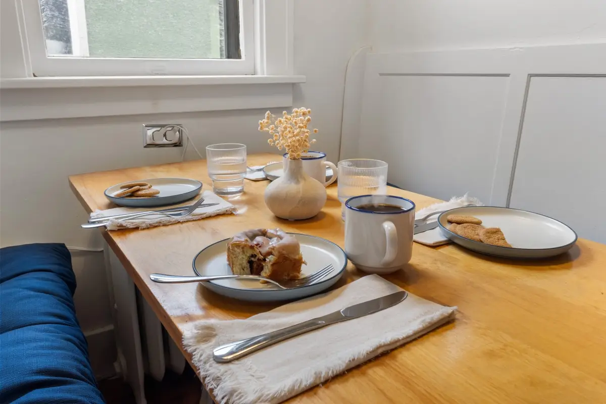 Breakfast nook table set with coffee, pastries, and a vase of dried flowers