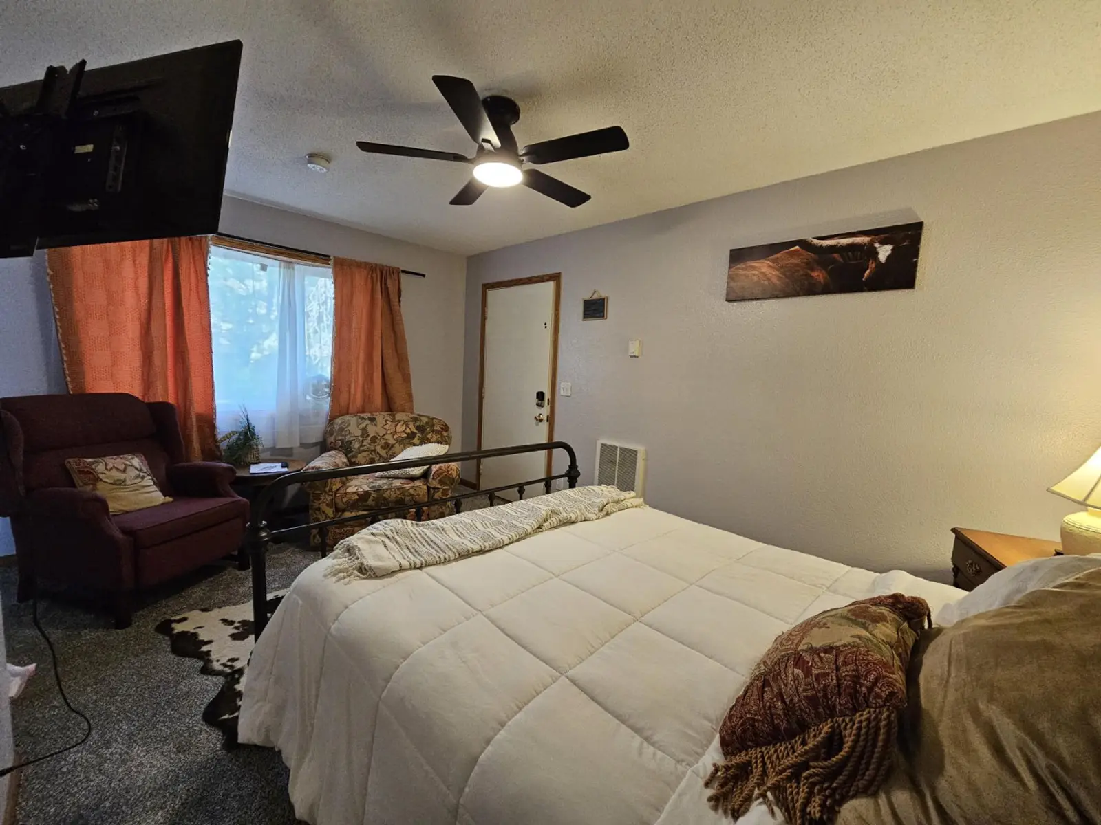 Studio with a queen bed, a ceiling fan, and orange curtains