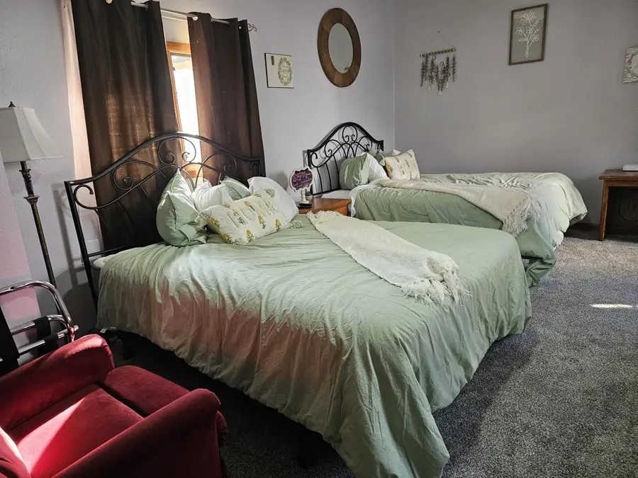 Two queen beds with iron headboards and a red armchair