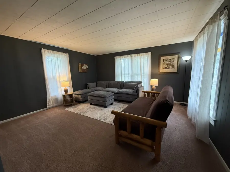Living room with a gray sectional and ottoman, a wood-frame futon, and sheer curtains