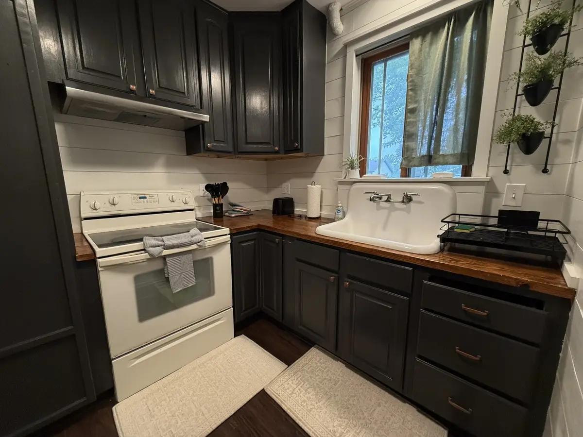 Kitchen corner with a white range, dark cabinets, and a farmhouse sink under a window