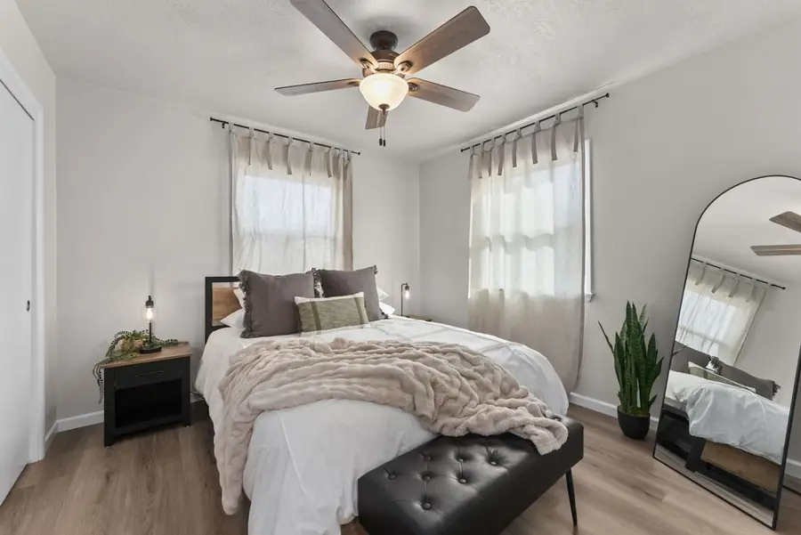 Bedroom with a queen bed, a black tufted bench, a ceiling fan, and an arched floor mirror