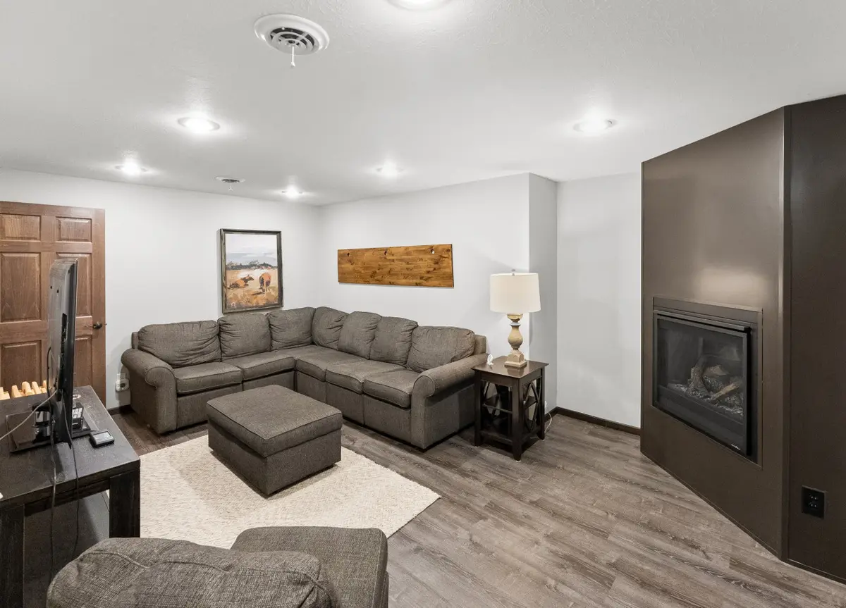 Den with a gray sectional, an ottoman, a TV, and a fireplace