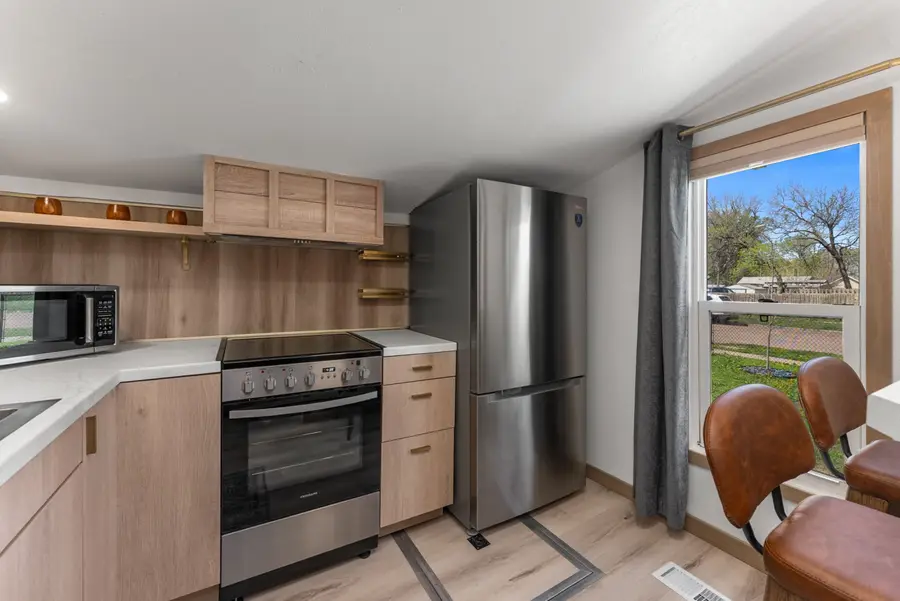 Kitchen with an electric range, stainless fridge, and wood cabinets by a window