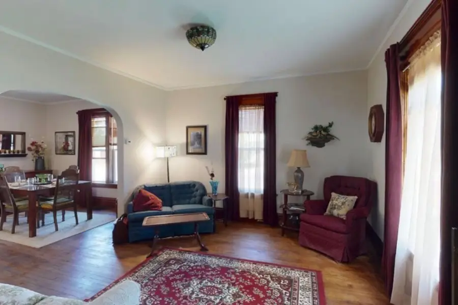 Living room with a blue sofa, a red armchair, and a patterned rug, with the dining room through an arch