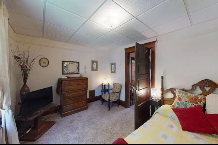 Bedroom with a carved wood headboard, a yellow quilt, a dresser, and a TV