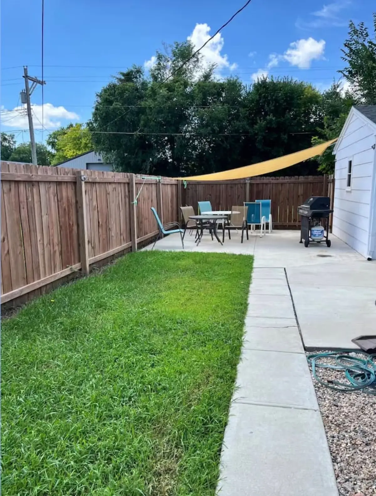 Backyard patio with a table and chairs under a shade sail, a grill, and a wood fence